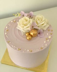 there is a pink cake with white roses and pearls on the top that has gold decorations