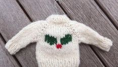 a knitted christmas sweater ornament hanging on a wooden fence with green and red decorations