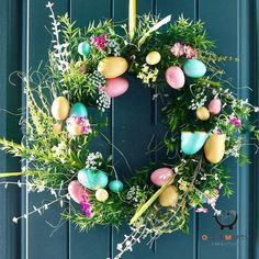 an easter wreath with eggs and flowers hanging on the front door, decorated with greenery