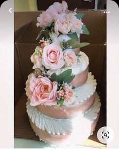 a three tiered wedding cake with pink flowers on the top and bottom, sitting in a cardboard box