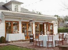 an outdoor dining area with white table cloths and wooden chairs set up in front of a house