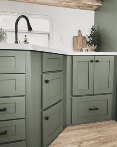 a kitchen with green painted cabinets and white counter tops, wood flooring in the middle