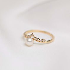 a pearl and diamond ring sitting on top of a white surface with a gold band