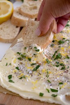 someone is dipping cheese onto bread with herbs on it and lemons in the background