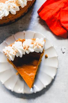 a slice of pumpkin pie on a white plate with whipped cream and an orange napkin