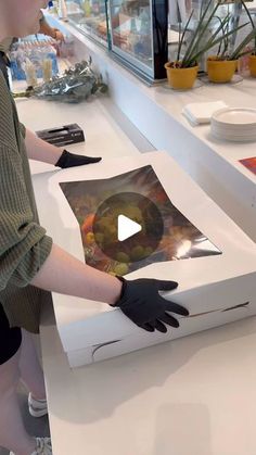 a woman in black gloves standing next to a white box with pictures on the side