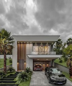 two cars are parked in front of a modern house with palm trees and landscaping on the lawn