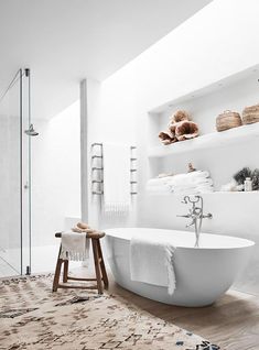 a white bath tub sitting on top of a wooden floor next to a shelf filled with towels