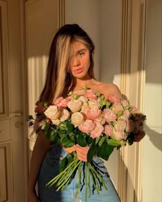 a woman holding a bouquet of flowers in her hands and looking at the camera while standing next to a door