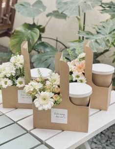 three brown paper bags with white flowers in them on a table next to some plants