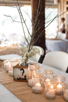 a table topped with lots of white candles and vases filled with flowers on top of it