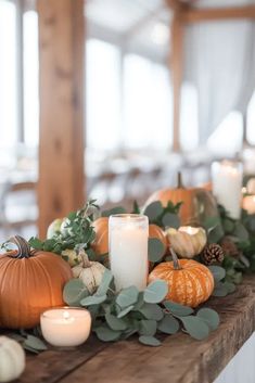 a table topped with candles and pumpkins on top of a wooden table covered in greenery