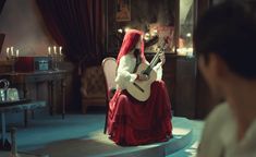 a woman sitting on a chair with a guitar in her hand and wearing a red dress