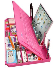 an open pink laptop computer sitting on top of a desk filled with assorted items