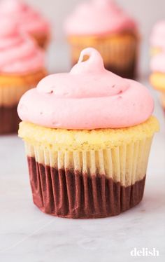 cupcakes with pink frosting on top sitting on a white countertop next to other cupcakes