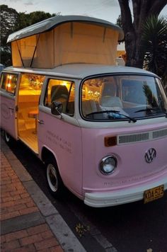 a pink and white van parked on the side of the road next to a tree