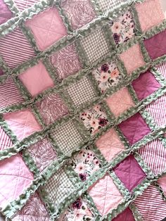 a pink and green patchwork quilt with flowers on the front, sitting on top of a bed