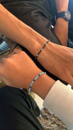 two people wearing bracelets sitting next to each other with their hands on the wrist