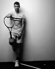 a man leaning against a wall holding a tennis racquet