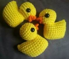 four crocheted yellow ducks sitting on top of a gray surface with black eyes