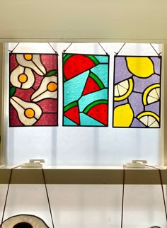 three colorful stained glass windows hanging from the side of a wall next to a window sill