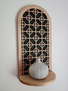 a white vase sitting on top of a wooden shelf next to a black and white wall