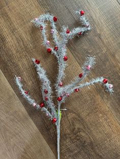 a small silver tree with red berries on it's branches, sitting on a wooden floor