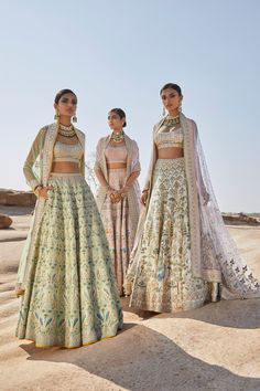 two women in matching outfits standing next to each other on the desert floor, one wearing a white and green lehenga