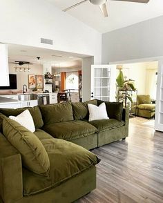 a living room filled with green couches and white walls in front of an open kitchen