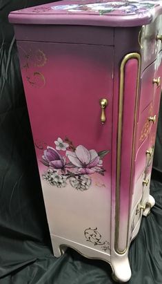 a pink and white cabinet with flowers painted on the front, sitting on a black background