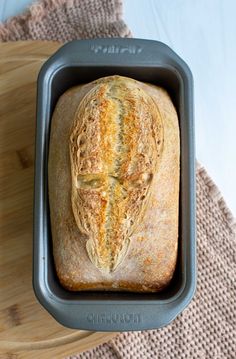 a loaf of bread sitting in a pan on top of a wooden table next to a cutting board