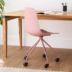 a pink chair sitting on top of a wooden floor next to a desk with a plant