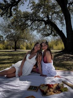 two young women sitting on a blanket under a tree