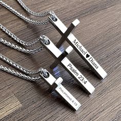 three personalized cross pendants with names on them sitting on a wooden table next to each other