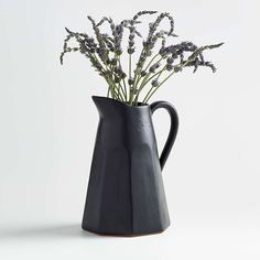 a black vase filled with purple flowers on top of a white table