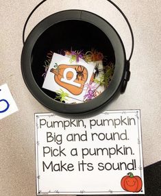 a black bucket filled with pumpkins next to a sign that says pumpkin, pumpkin big and round pick a pumpkin make it's sound