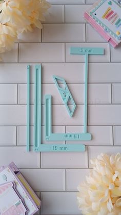 a white tile wall with some flowers and scissors on it, next to a ruler