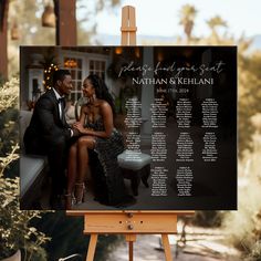 a couple is sitting on a bench in front of a black and white wedding seating chart