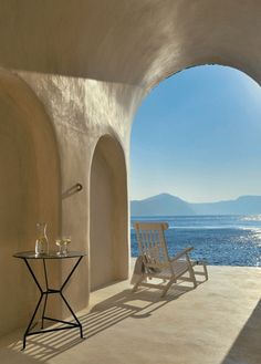 a chair sitting on top of a stone floor next to an arch over looking the ocean