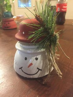 a snowman jar sitting on top of a wooden table next to a potted plant