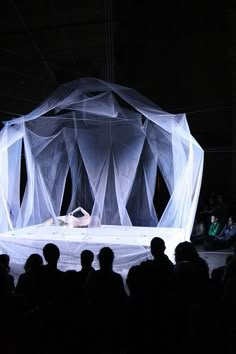 a group of people standing around a stage with white drapes on it's sides