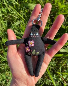 a hand holding a black stuffed animal keychain with flowers on it's face