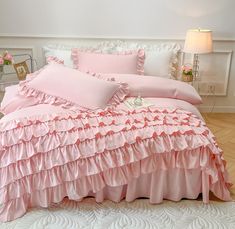 a bed with pink ruffles and pillows in a white room next to a lamp