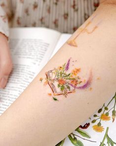 a woman's arm with flowers on it and an open book in the background