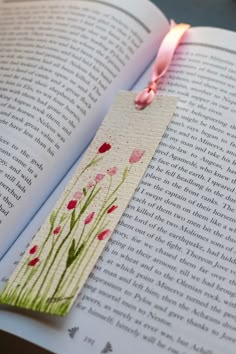 an open book with a pink ribbon and flowers on the page, next to a candle