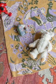 a white teddy bear sitting on top of a colorful rug next to a red toy