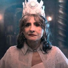 an older woman wearing a tiara and looking at the camera while standing in front of a mirror