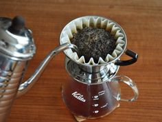 a coffee pot filled with black stuff on top of a wooden table next to a cup