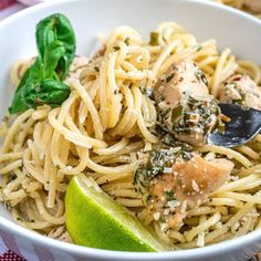 a white bowl filled with pasta and meat next to a slice of green leafy garnish