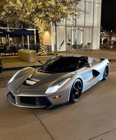 a silver sports car is parked in front of a building at night with lights on